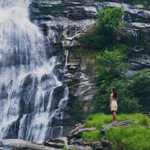 A fascinating low angle shot of a female admiring the waterfall in Doi Inthanon park in Thailand
